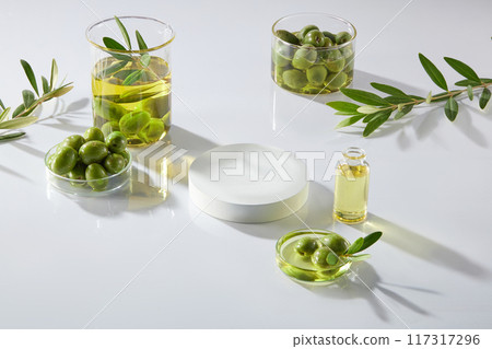On the white background, beaker and petri dishes filled with olives, olives oil and leaves decorated. A white empty podium for display product with ingredient from olive On the white background, beaker and petri dishes filled with olives, olives oil and leaves decorated. A white empty podium for display product with ingredient from olive 117317296
