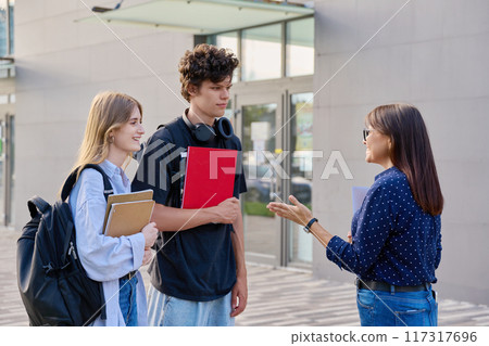 Group of college students talking with female teacher, educational building background 117317696