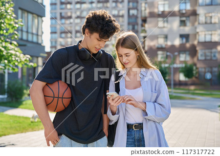 Young teenage guy and girl walking, looking at smartphone together, urban background Young teenage guy and girl walking, looking at smartphone together, urban background 117317722