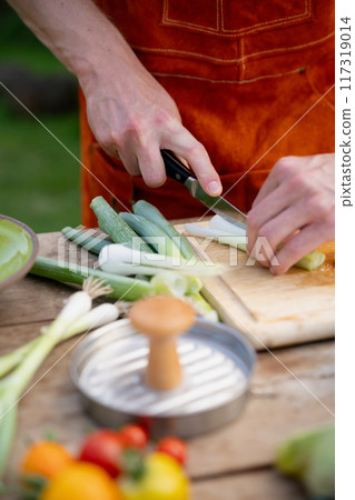Close up of man holding sharp knife, cutting spring onion. Preparing vegetables for an outdoor barbecue. Close up of man holding sharp knife, cutting spring onion. Preparing vegetables for an outdoor barbecue. 117319014