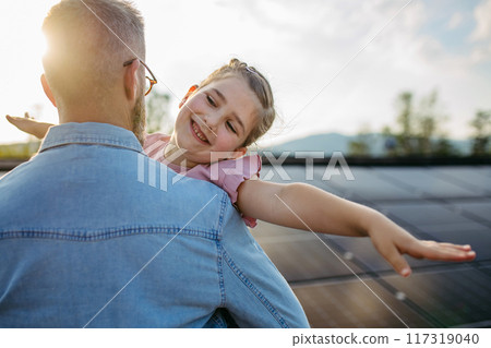 Father with girl on roof with solar panels, hugging. Rooftop solar or photovoltaic system. Sustainable future for next generation. 117319040