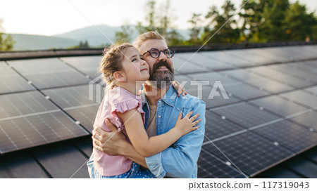 Father with girl on roof with solar panels, hugging, looking at the sky. Rooftop solar or photovoltaic system. Sustainable future for next generation. Father with girl on roof with solar panels, hugging, looking at the sky. Rooftop solar or photovoltaic system. Sustainable future for next generation. 117319043