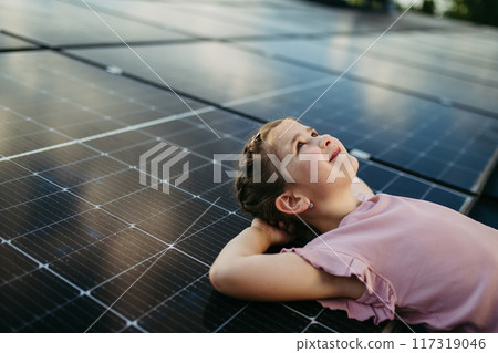 Cute girl lying on solar panels roof, shot with copy space. Rooftop solar or photovoltaic system. Sustainable future for next generation. Cute girl lying on solar panels roof, shot with copy space. Rooftop solar or photovoltaic system. Sustainable future for next generation. 117319046