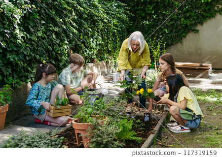 Students and female teacher at outdoor sustainable education class. Kids taking care of plants in school garden. Concept of experiential learning and ecoliteracy. Students and female teacher at outdoor sustainable education class. Kids taking care of plants in school garden. Concept of experiential learning and ecoliteracy. 117319159
