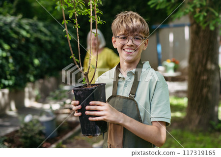 Young student boy holding fruit tree seedling. Kids taking care of school garden during outdoor sustainable education, class in forest school. Concept of experiential learning and ecoliteracy. 117319165