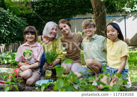 Portrait of students and female teacher at outdoor sustainable education class. Planting vegetable seedling, herbs in soil. Concept of experiential learning and ecoliteracy. 117319168