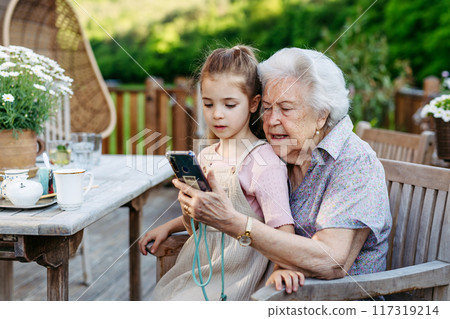 Granddaughter taking selfie with elderly grandma, companionship. Senior lady spending time with young girl, enjoying together time. Granddaughter taking selfie with elderly grandma, companionship. Senior lady spending time with young girl, enjoying together time. 117319214