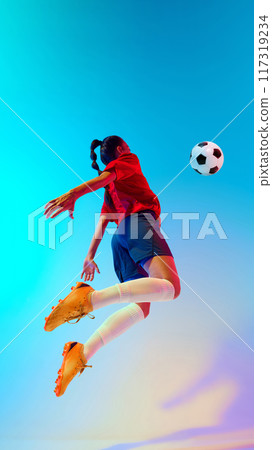 Soccer player leaps gracefully, arms outstretched, prepare to strike ball in neon light against colorful gradient background. 117319234