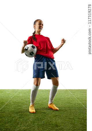 Full-length photo of young, female football athlete celebrates game-changing moment standing on stadium with ball and shouting of joy. 117319278