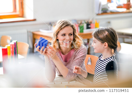 Hardworking teacher learning with young schoolgirl in classroom, explaining math problem, using education tools. Hardworking teacher learning with young schoolgirl in classroom, explaining math problem, using education tools. 117319451
