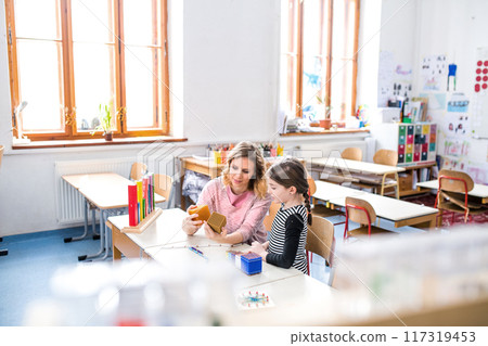Hardworking teacher learning with young schoolgirl in classroom, explaining math problem, using education tools. Hardworking teacher learning with young schoolgirl in classroom, explaining math problem, using education tools. 117319453