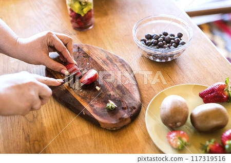 Overweight woman in the kitchen, making fresh smoothie. Choosing healthy food, cutting fruit on cutting board. Overweight woman in the kitchen, making fresh smoothie. Choosing healthy food, cutting fruit on cutting board. 117319516