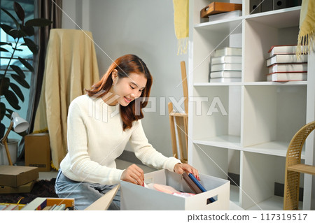 Happy young woman moving in new house and unpacking cardboard boxes 117319517