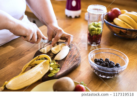 Overweight woman in the kitchen, making fresh smoothie. Choosing healthy food, cutting fruit on cutting board. Overweight woman in the kitchen, making fresh smoothie. Choosing healthy food, cutting fruit on cutting board. 117319518