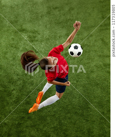Aerial view of young athletic woman, football defender wearing comfortable uniform hitting ball with chest in mid air. 117319805