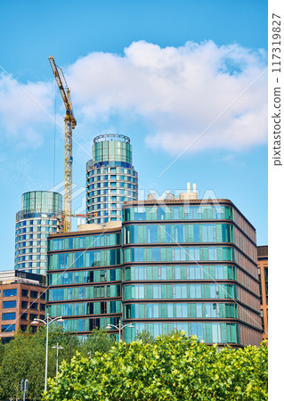 Glass and steel office buildings in business district. Modern urban architecture under construction. Construction crane building real estate in city Glass and steel office buildings in business district. Modern urban architecture under construction. Construction crane building real estate in city 117319827