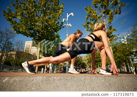 Shirtless muscular man and sportive woman in black sportswear doing warming up, stretching exercises before intense outdoor training session Shirtless muscular man and sportive woman in black sportswear doing warming up, stretching exercises before intense outdoor training session 117319873