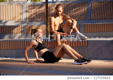 Sportive man and woman enjoying early summer morning training session in public city place, training, doing press exercises 117319928