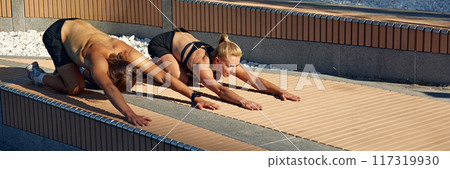 Sportive young people, man and woman training outdoors, doing stretching, Pilates, yoga exercises in early summer morning 117319930