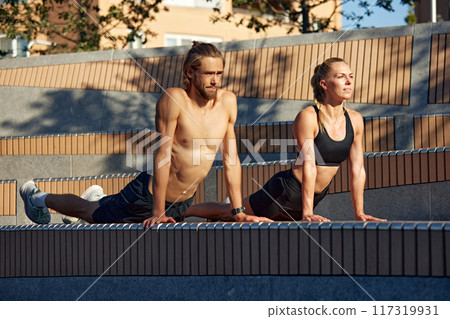 Sportive young people, man and woman training outdoors, doing stretching, Pilates, yoga exercises in early summer morning Sportive young people, man and woman training outdoors, doing stretching, Pilates, yoga exercises in early summer morning 117319931