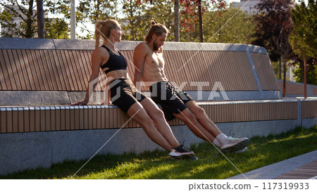 Sportive people, man and woman training outdoors in early summer morning, doing reverse push ups exercises, workout out in public park 117319933