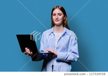 Smiling teenage girl with laptop on blue studio background 117320556