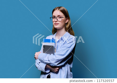 Portrait female college student holding textbooks tablet on blue background 117320557