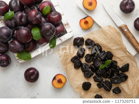 Dried sweet prunes with ripe plums in wooden box on light kitchen background. 117320751