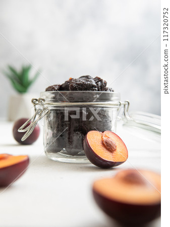 Dried sweet prunes in glass jar on light background with plum halves. 117320752