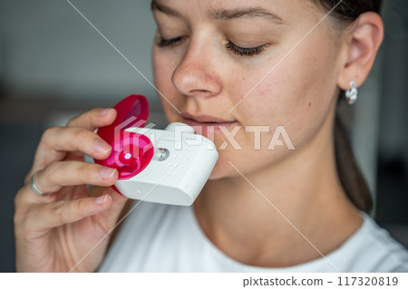 Close up view of woman using medicine dry powder inhaler for treatment asthma or COPD diseases. Pharmaceutical product is used to treat lung inflammation and prevent asthma attack. 117320819