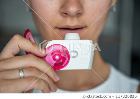 Close up view of woman using medicine dry powder inhaler for treatment asthma or COPD diseases. Pharmaceutical product is used to treat lung inflammation and prevent asthma attack. 117320820