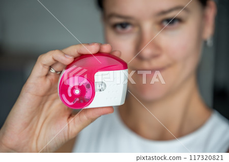 Close up view of woman holding medicine dry powder inhaler for treatment asthma or COPD diseases. Pharmaceutical product is used to treat lung inflammation and prevent asthma attack. Close up view of woman holding medicine dry powder inhaler for treatment asthma or COPD diseases. Pharmaceutical product is used to treat lung inflammation and prevent asthma attack. 117320821