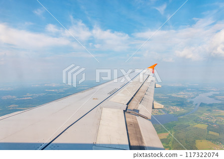 View of airplane wing, blue skies and green land during landing. Airplane window view. View of airplane wing, blue skies and green land during landing. Airplane window view. 117322074