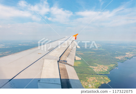 View of airplane wing, blue skies and green land during landing. Airplane window view. 117322075
