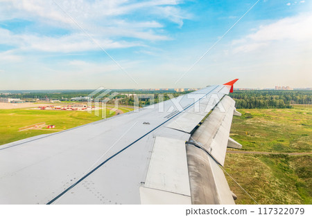 View of airplane wing, blue skies and green land during landing. Airplane window view. View of airplane wing, blue skies and green land during landing. Airplane window view. 117322079
