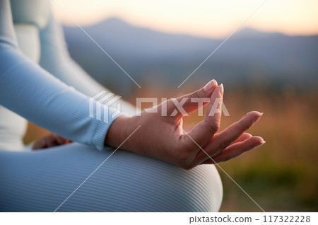 Close up of woman's hands on dawn background in the evening. Woman doing yoga exercise and meditating during sunset in mountains 117322228