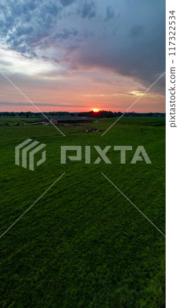 A stunning sunset casts vibrant colors over green fields, creating a serene atmosphere A stunning sunset casts vibrant colors over green fields, creating a serene atmosphere 117322534