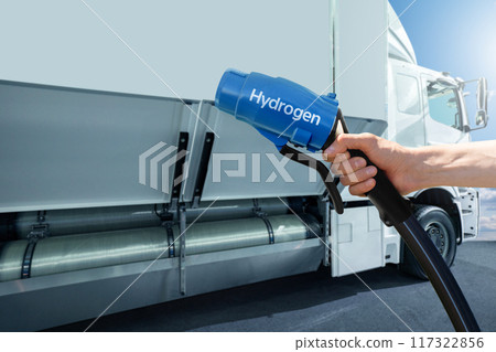 Hand with H2 nozzle on a background of hydrogen fuel cell semi truck with H2 gas cylinder onboard. Eco-friendly commercial vehicle concept. Hand with H2 nozzle on a background of hydrogen fuel cell semi truck with H2 gas cylinder onboard. Eco-friendly commercial vehicle concept. 117322856