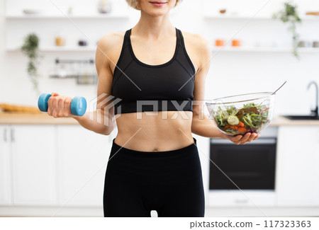 Woman holding dumbbell salad in modern kitchen 117323363