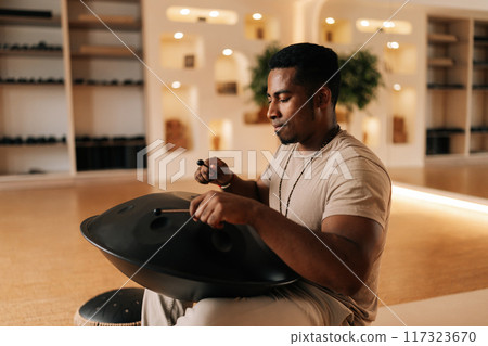 Meditate African man in trance enjoying playing ethnic music on glucophone using sticks sitting on floor in lotus pose. Concept of mindfulness, tranquility, harmony, sound therapy. Meditate African man in trance enjoying playing ethnic music on glucophone using sticks sitting on floor in lotus pose. Concept of mindfulness, tranquility, harmony, sound therapy. 117323670