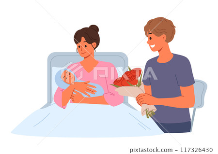 Woman who has given birth lies in hospital bed, showing baby to happy father with flowers 117326430