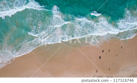 Aerial view of a sandy beach with turquoise waves crashing onto the shore scattered people are seen walking along the coastline 117328746
