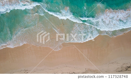 Aerial view of a sandy beach with turquoise waves crashing onto the shore scattered people are seen walking along the coastline Aerial view of a sandy beach with turquoise waves crashing onto the shore scattered people are seen walking along the coastline 117328748