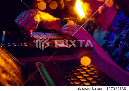 DJ's hands work mixer, bathed in ambient glow of stage lights, shaping rhythm that will move crowd. DJ's hands work mixer, bathed in ambient glow of stage lights, shaping rhythm that will move crowd. 117329188