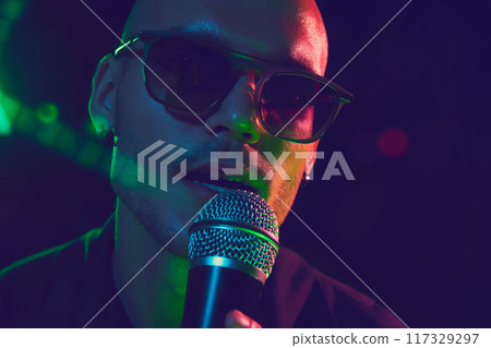 Close-up photo of singer's face, his expression full of intensity and passion, bathed in neon lights during powerful performance. 117329297