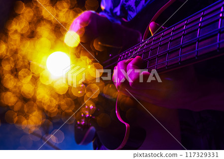 Glow of stage lights highlights movement of guitarist's hand, creating dynamic visual of live music moment. Glow of stage lights highlights movement of guitarist's hand, creating dynamic visual of live music moment. 117329331