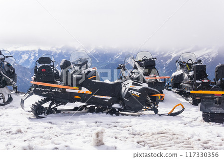 Snowmobiles in the snow in the highlands against the background of a blue sky with white clouds. 117330356