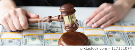 Woman judge holding wooden gavel, pile of dollars on table 117331074
