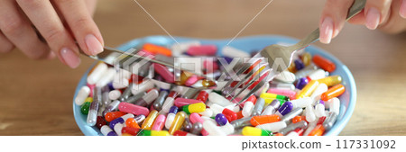 Female hands holding fork and knife and pills in heart-shaped bowl Female hands holding fork and knife and pills in heart-shaped bowl 117331092