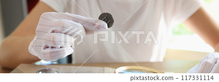 Woman numismatist examining coin with magnifier Woman numismatist examining coin with magnifier 117331114